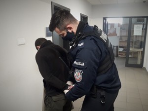 Policjant zakłada kajdanki na ręce zatrzymanemu mężczyźnie