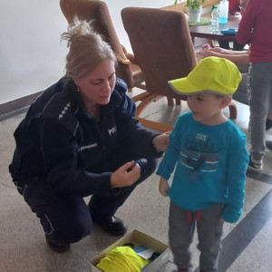 Policjantka przyklęka przy dziecku i zakłada mu czapkę z daszkiem.