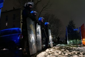 Policjanci z oddziału prewencji stoją z tarczami przy wejściu do stadionu.