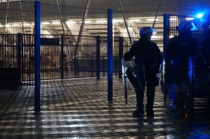 Widok na kratę oddzielającą stadion od drogi, obok stoją policjanci z prewencji.