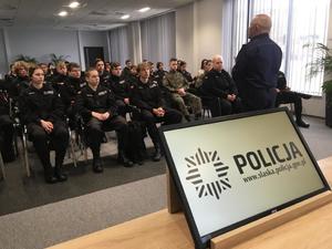 Młodzież klas średnich siedzi na sali konferencyjnej komendy, na pierwszym planie policjant prowadzą prelekcję.