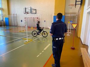 Policjanci z ruchu drogowego prowadzą turniej na sali gimnastycznej, uczniowie na rowerach pokonują tor przeszkód.