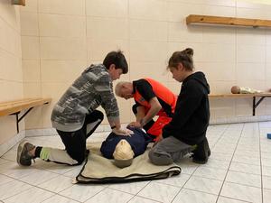 Uczniowie wykonują zadania podczas konkursu z udzielania pierwszej pomocy, ratownik medyczny przygląda się ich czynnościom.