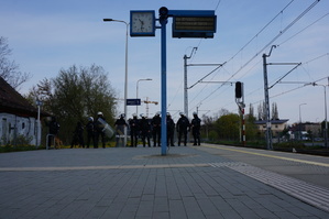Na pierwszym planie zegar kolejowy, w tle policjanci w rynsztunku bojowym
