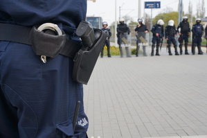 Zbliżenie na kaburę z policyjnym pistoletem Walther P99, w tle policjanci stojący w szeregu