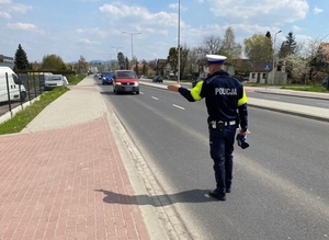 Policjant stoi na jezdni i zatrzymuje pojazd do kontroli.