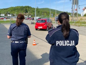 Policjantka obserwuje jazdę konkursową czerwonym pojazdem na placu manewrowym.