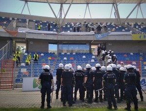 Policjanci z oddziałów prewencji w rynsztunku bojowym ćwiczą działania na stadionie.