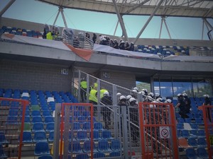 Policjanci z oddziałów prewencji w rynsztunku bojowym ćwiczą działania na stadionie.