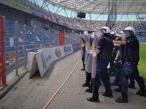 Policjanci z oddziałów prewencji w rynsztunku bojowym ćwiczą działania na stadionie.