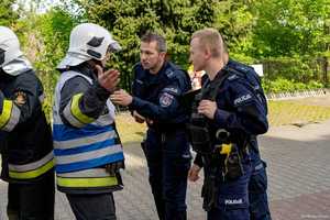 Umundurowani policjanci rozmawiają ze strażakiem w kamizelce dowódcy działań ratowniczych.