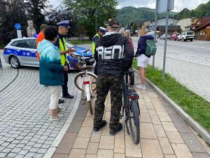 Policjanci rozmawiają z rowerzystami podczas akcji profilaktycznej, w tle góry i pochmurne niebo.