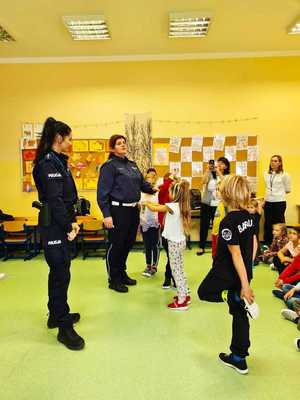 Dwie policjantki stoja w klasie, obok nich stoją dzieci.