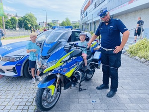 Na zdjęciu na motosyklu siedzi dziecko, obok niego stoi policjant.
