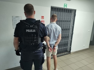 zdjęcie kolorowe przedstawiające dwóch policjantów wraz z zatrzymanym mężczyzną na korytarzu