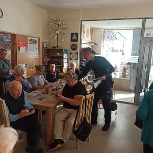 na zdjęciu policjant obok siedzących przy stole seniorach