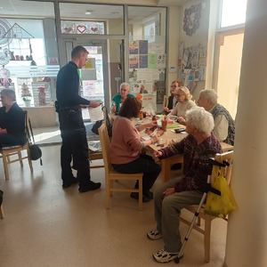 na zdjęciu policjant, obok niego siedzących przy stole seniorzy